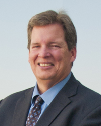 Close-up photo of Ed Hart wearing a dark gray suit and blue shirt.