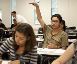 Student in brown t-shirt raises hand during class.