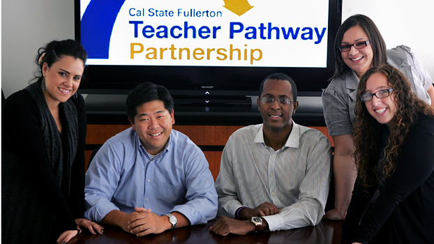 Five individuals around a table and before a sign that reads “Teacher Pathway Partnership.”