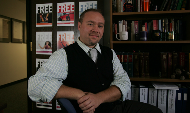 Jason Shepard stands in his office in front of a door covered with signs about freedom of the press.