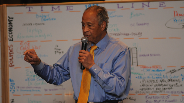 President Milton A. Gordon is shown before a white board and speaking to a university group.