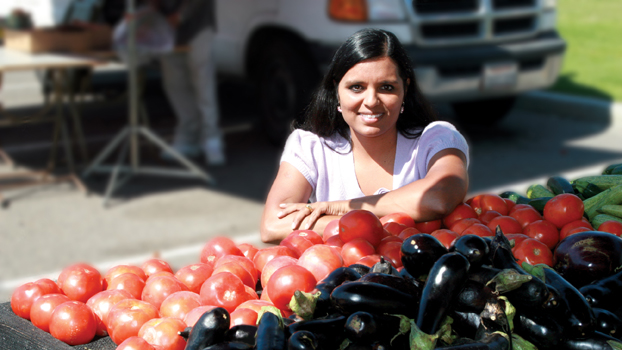 Archana McEligot stands behind a gigantic bin of tomatos and eggplant.