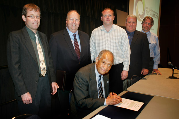 President Milton A. Gordon signs international agreement surrounded by faculty, staff and a student.