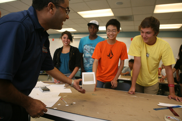 Binod Tiwari, forefront, shows an example of a mousetrap made with paper and glue to a group of students.