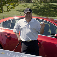 Tony Saucedo holds winning golf ball and stands infront of the car he won.