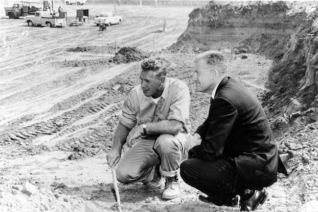 President Langsdorf crouches beside contract to oversee ground being cleared for the future university.