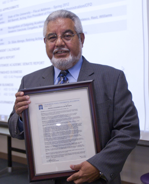 salt-and-pepper haired gentleman in a gray suit holding a framed resolution.