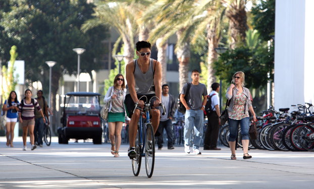 A lone biker rides into the heart of campus; behind him are walkers.