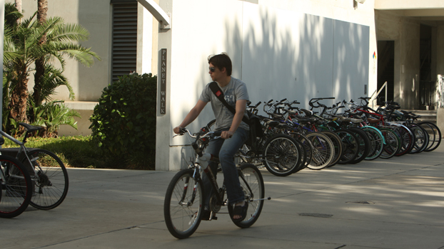 A student riding a bicycle pass bike racks and McCarthy Hall.