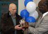 black man in a suit hands a crystal elephant to another gentleman