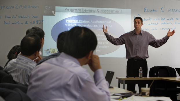 A group of Vietnamese educators listen to John Hoffman in front of a white board.