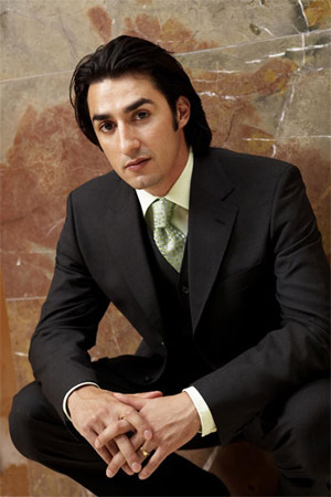 Charles Castronova, in business suit, crouching infront of a marble wall.