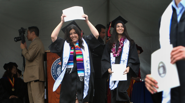 Hispanic student throws her arms in the air after receiving her diploma.