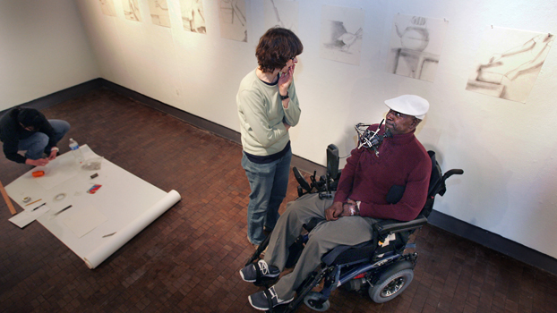 Man in wheelchair talks to a woman standing next to him.