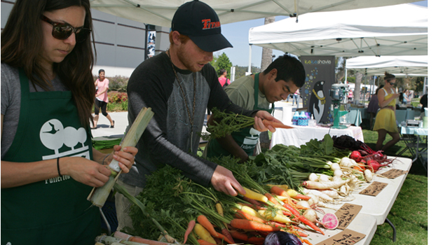 A woman and two men prepare fresh vegetables and fruit for sale.