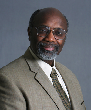 Portrait photo showing black man wearing a light beige suit and glasses.