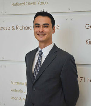 Anthony Kress in a suit and tie, standing before a donors board located in Mihaylo Hall.