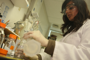female student pours chemicals from a beaker into a glass jar.