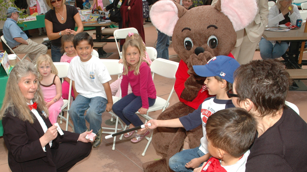 blond woman in a black suit performs a card trick for younsters during a previous literacy festival.