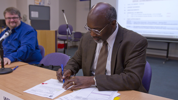 Black man in a business suit signs a document.