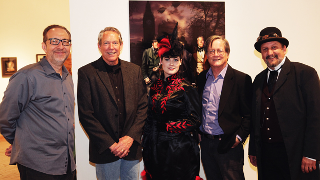 five people, some in costume, stand before an illustration that is part of the Steampunk exhibit.