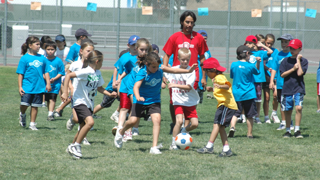 Youngsters chase a soccer ball under the direction of a camp counselor