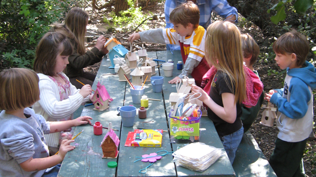 children at a wood picnic table painting wooden birdhouses.