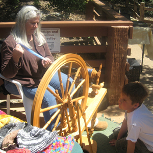 A gray-haired woman spins thread on a spinning wheel.
