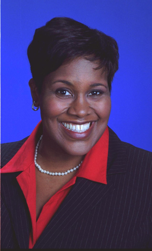 Black woman in a red shirt and black suit posed in front of a bright blue background