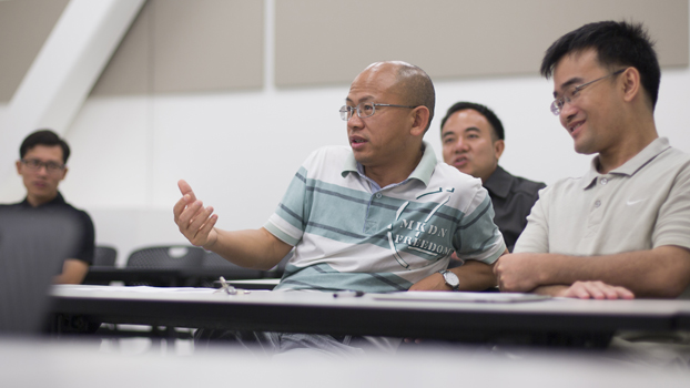 Four Chinese educators hold a discussion in a classroom.