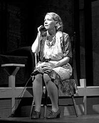 A woman on stage, dressed as a 1950s housewife, answers the telephone.