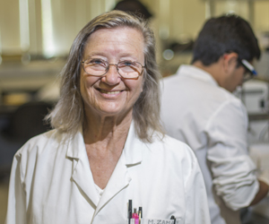 woman wearing lab coat standing in front of students working in the lab.