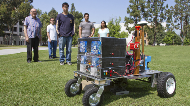 Four men and a woman stand behind a square-robotic lawn mower.