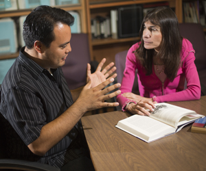 A man gestures with his hands while talking to a woman in a pink sweater.