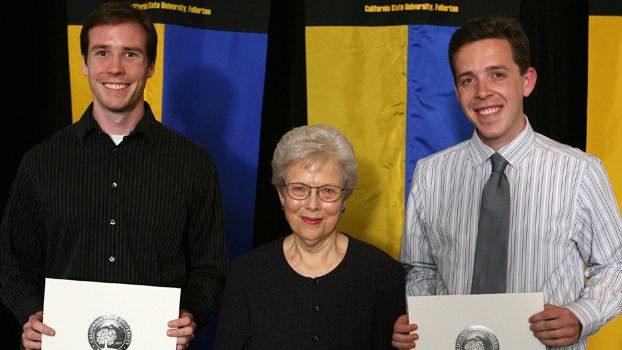 Two young men holding certificates flank an elderly woman.