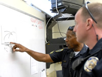Two uniformed police officers standing at a whiteboard discussing a campus safety exercise.