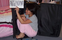 Doreen crouching within her suitcase with a sign displaying "Argentina"