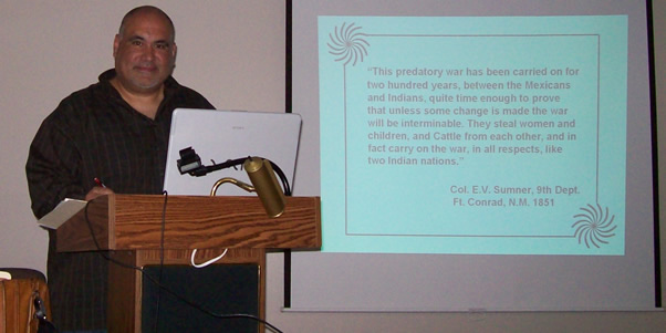 Robert Castro standing at a podium delivering a multimedia-aided lecture.