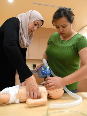Two nursing students practice with equipment in a lab