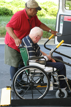 Elderly man in wheelchair being assisted into a vehicle