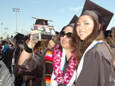 Two graduates pose for pictures in the crowd during commencement